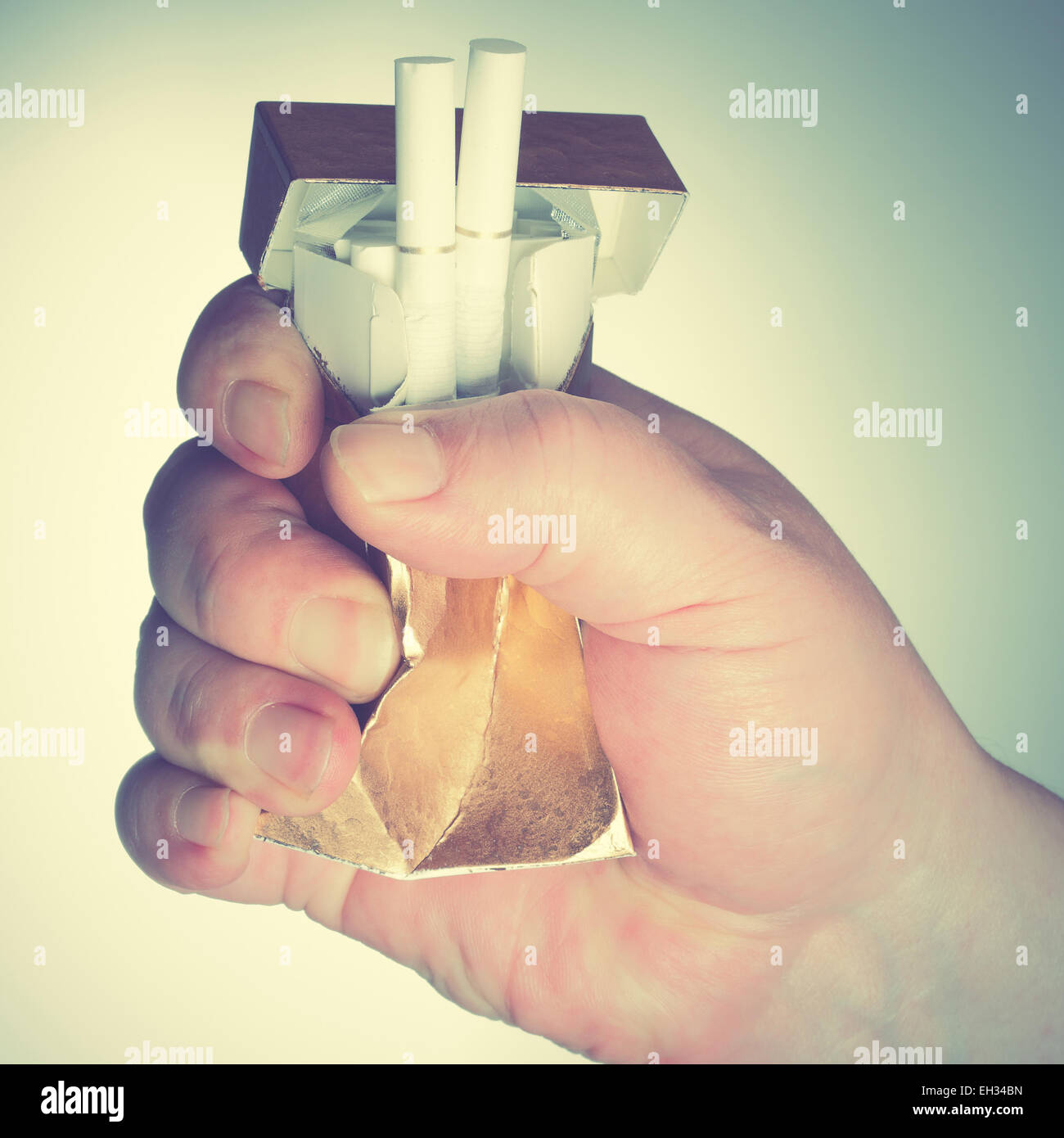 Man's hand crushing cigarette box. Retro style filtred image Stock Photo