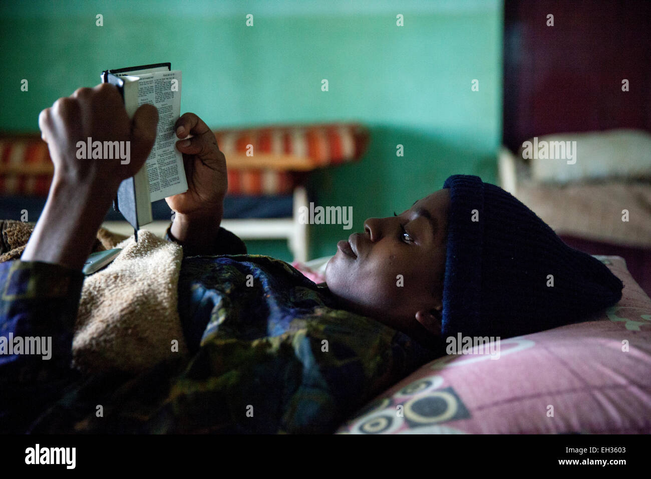 Bamenda, Cameroon, July 2013; A young woman, sick with a serious illness, reading the bible in a hospital bed. Stock Photo