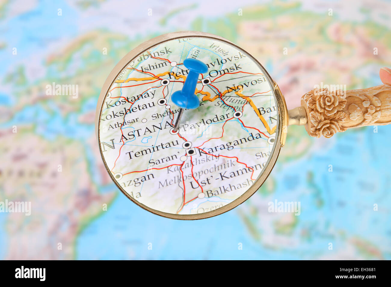 Blue tack on map of the world with magnifying glass looking in on Astana, Kazakhstan Stock Photo