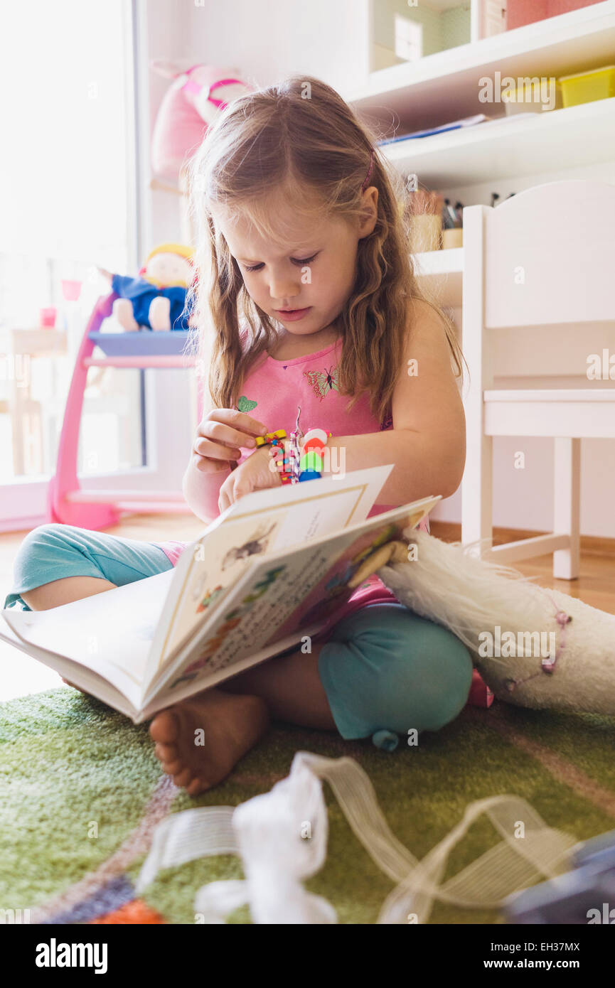 Little Girl Sitting on the Floor of her Bedroom, Reading a Book and ...