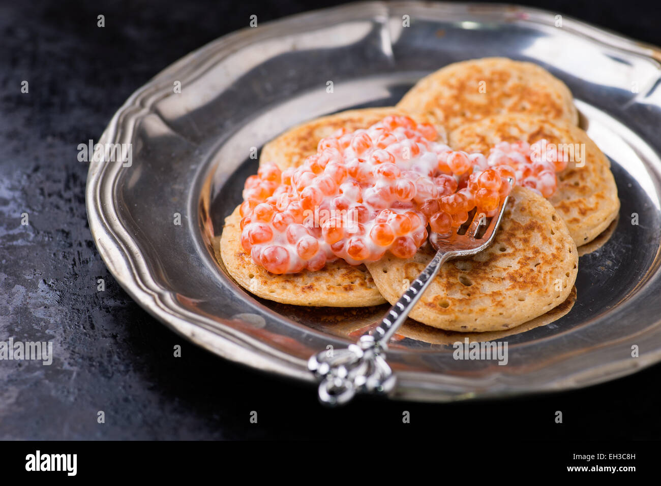 Buckwheat blini with red caviar and sour cream on metal plate