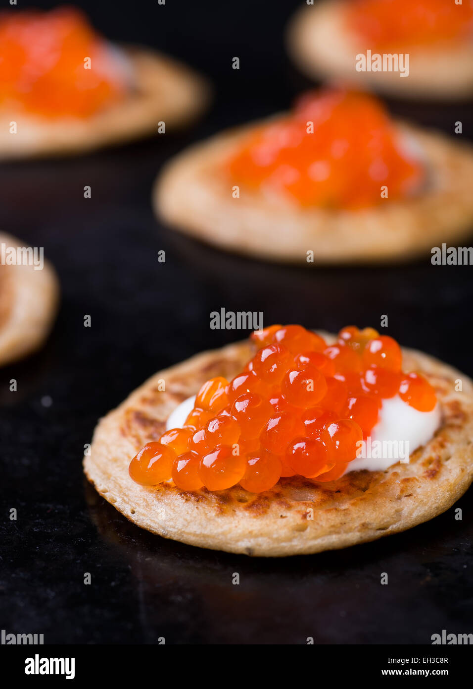 Buckwheat blini with red caviar and sour cream on dark background