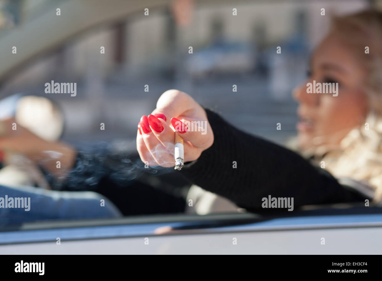 a driving blonde woman shakes down her cigarette's ash out the window