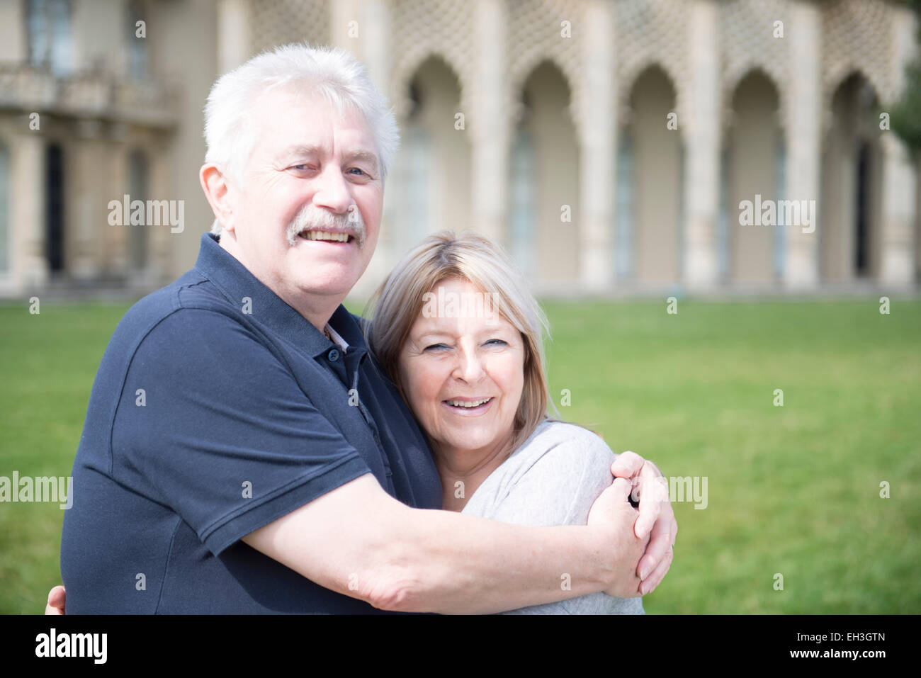 an elderly couple cuddle and embrace showing love in front of Brighton's tourist landmark the Royal Pavilion on the grass Stock Photo