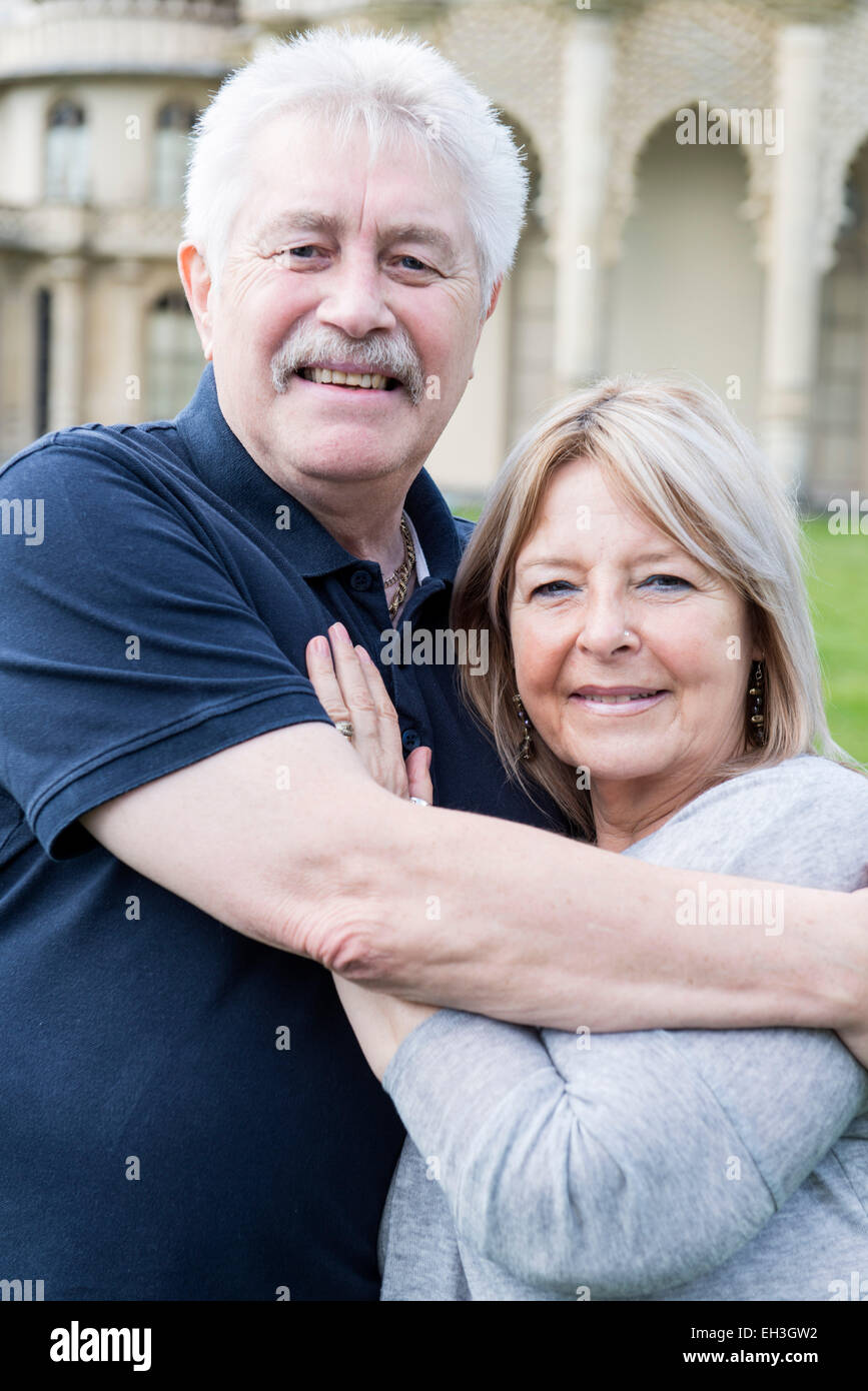 an elderly couple cuddle and embrace showing love in front of Brighton's tourist landmark the Royal Pavilion on the grass Stock Photo