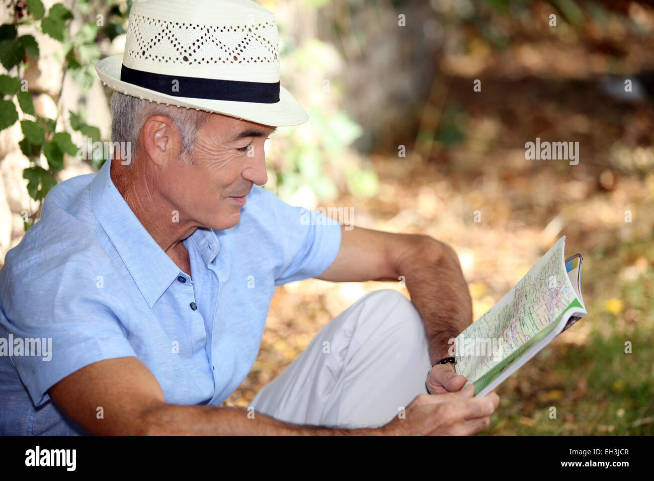 65 years old man sitting in the grass and watching a book Stock Photo