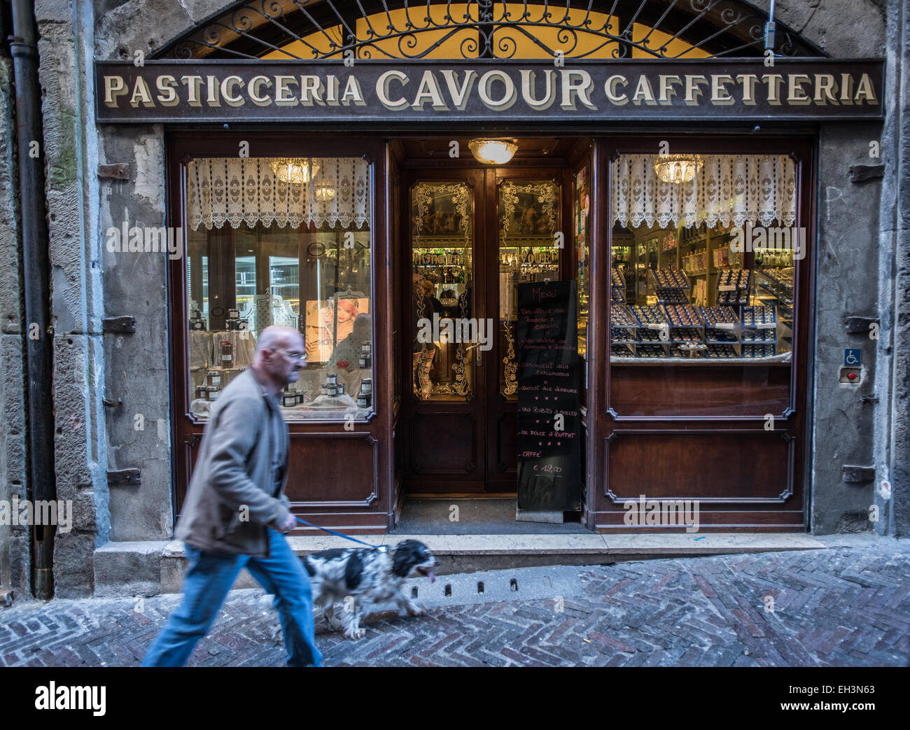 Bergamo, Italy - A man with a dog walks in front of pastry shop Pasticceria, Caffetteria Cavour in Via Gombito, in the old town Stock Photo