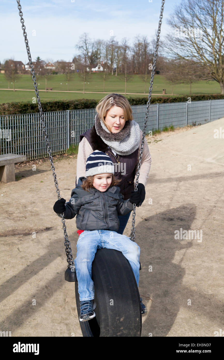 Mum pushing toddler on a swing in a playground Stock Photo
