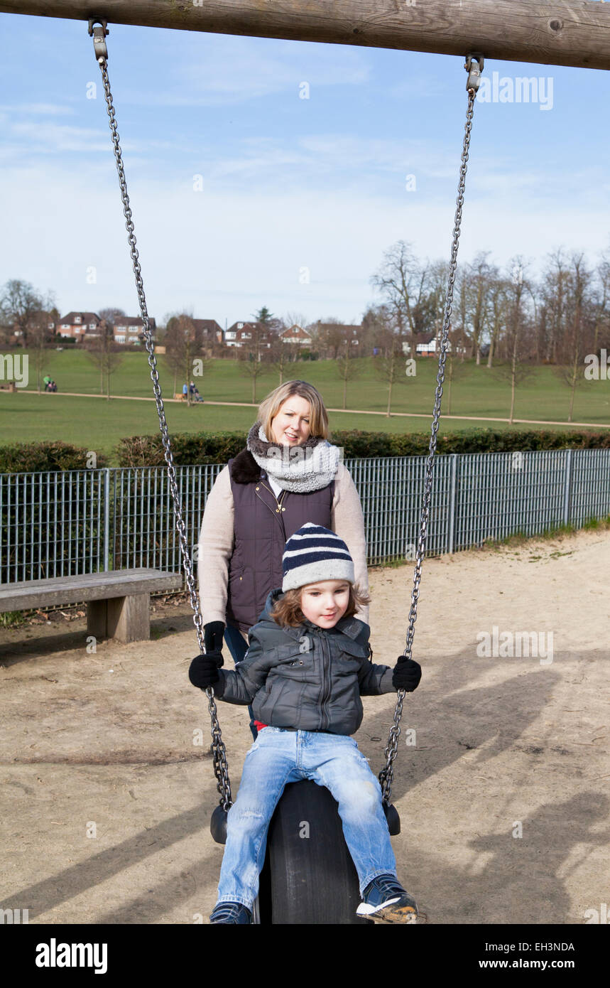 Mum pushing toddler on a swing in a playground Stock Photo