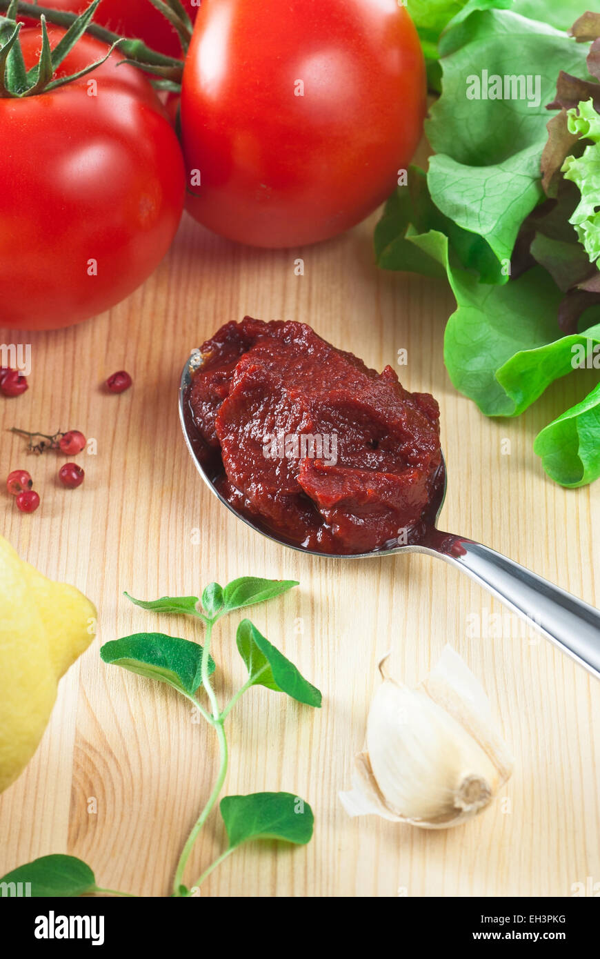 Tomato paste in a spoon. Fresh tomato, fresh oregano and pepper.  Everything on a plate. Stock Photo