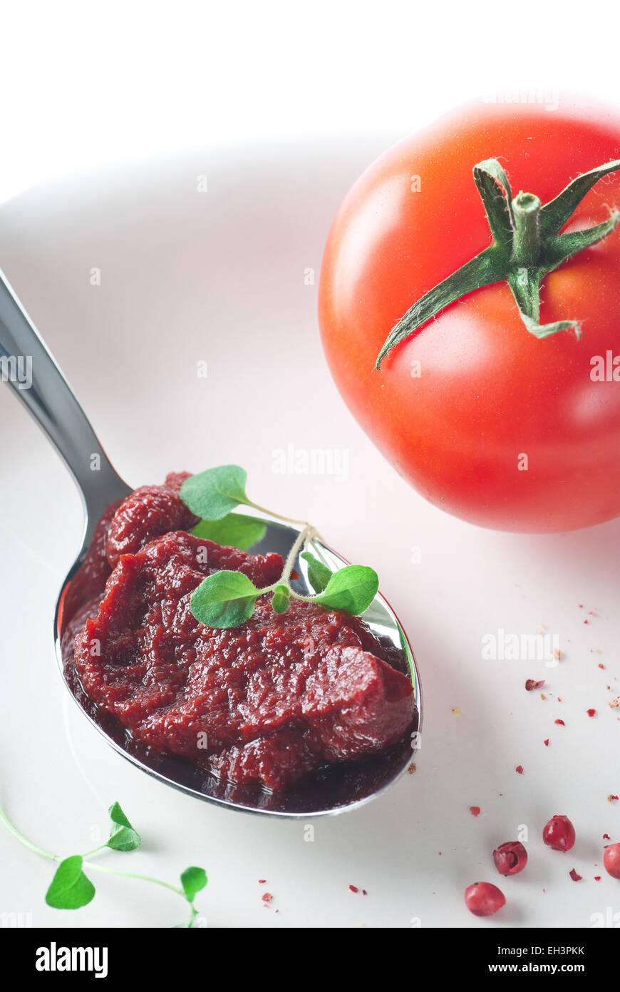 Tomato paste in a spoon. Fresh tomato, fresh oregano and pepper.  Everything on a plate. Stock Photo