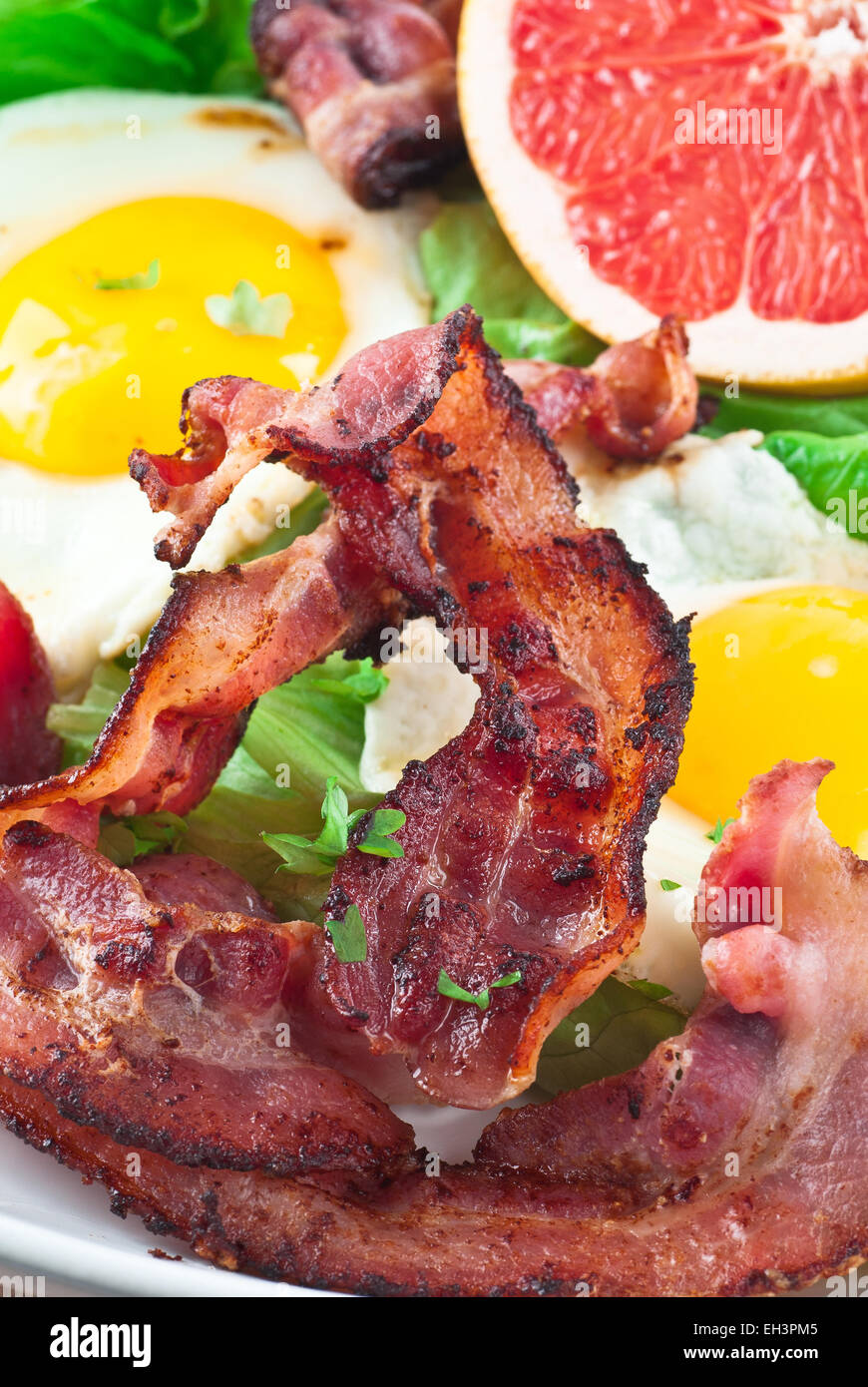 Bacon with fried eggs, lettuce and grapefruit. Stock Photo
