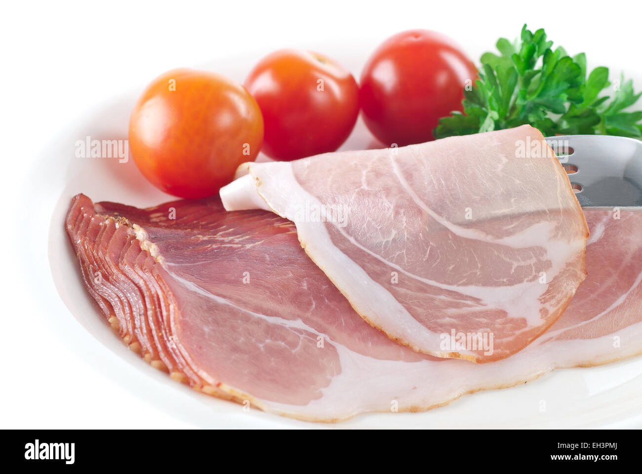 Sliced smoked ham garnished with tomato and parsley. Stock Photo