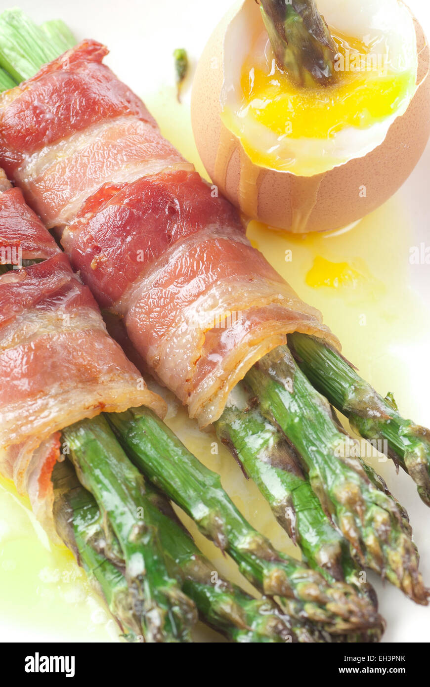 Oven baked bacon wrapped asparagus, served with melted butter and boiled egg. Stock Photo