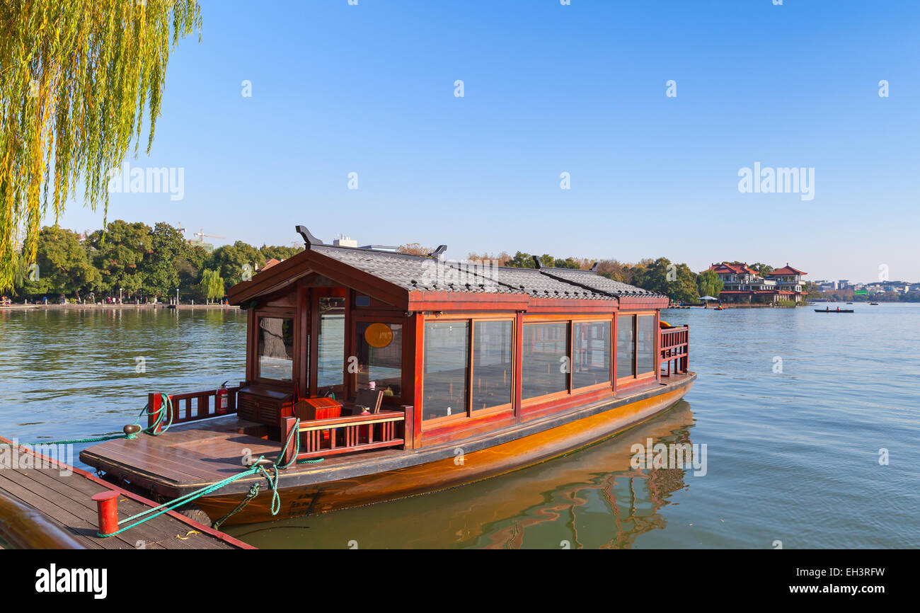 Traditional Chinese red wooden water taxi boat stands moored on the West Lake coast. Famous park in Hangzhou city center, China Stock Photo