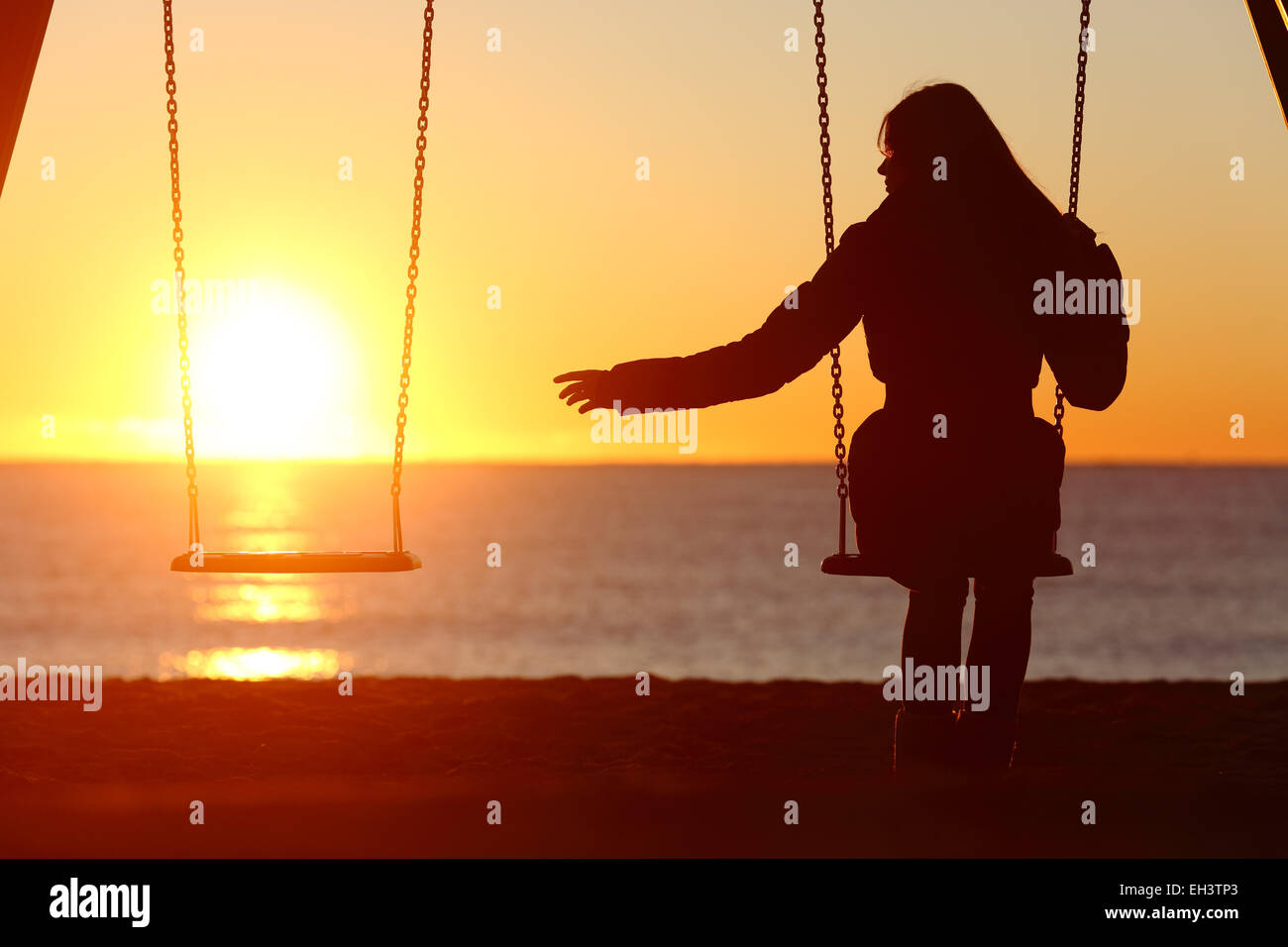 Single or divorced woman alone missing a boyfriend while swinging on the beach at sunset Stock Photo