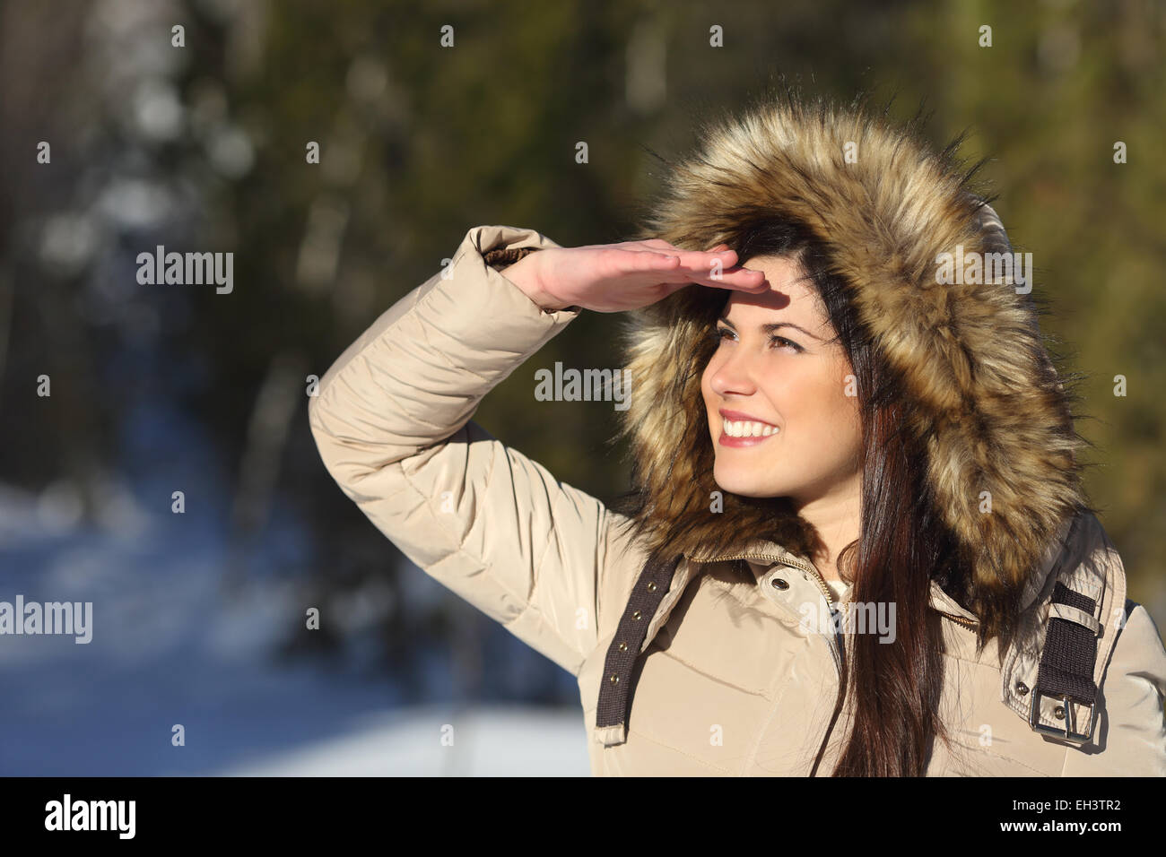 Woman looking forward with the hand on forehead in a forest in winter holidays Stock Photo
