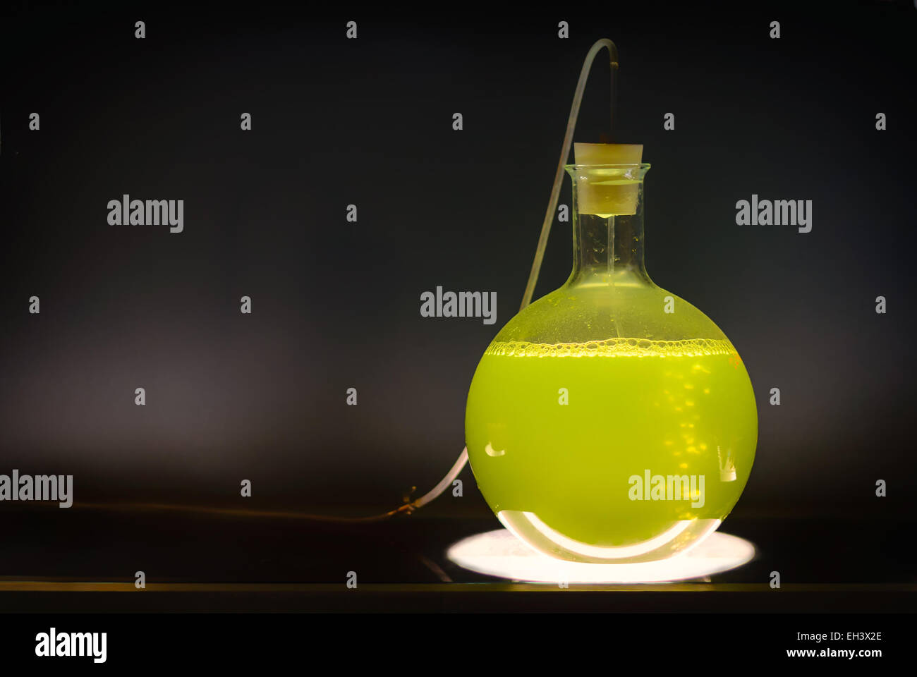 Volumetric flask with green liquid in experiment in dark room laboratory, chemical reaction, distillation. Stock Photo