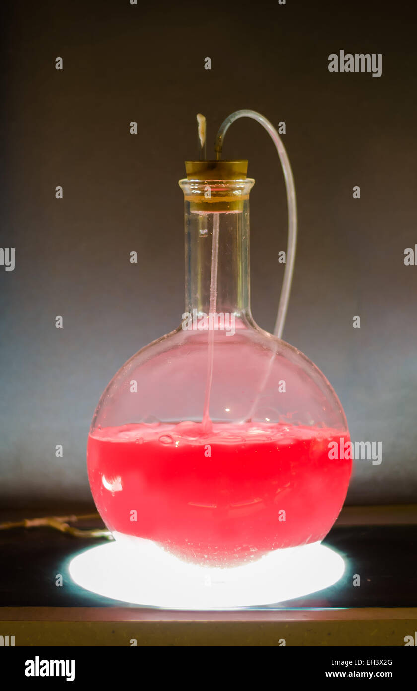 Volumetric flask with pink liquid in experiment in dark room laboratory, chemical reaction, distillation. Stock Photo