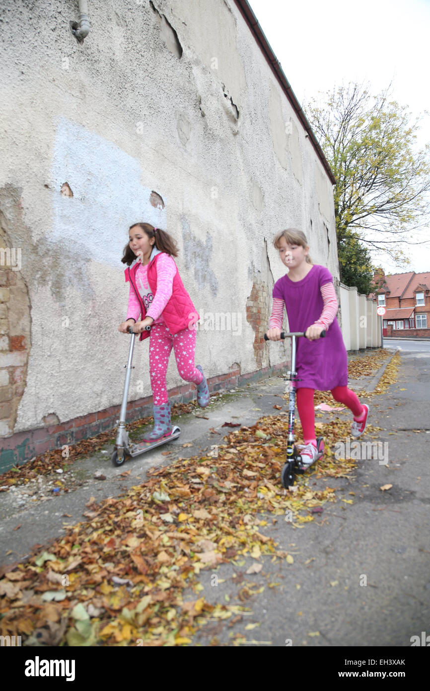 Girls playing on scooters in street Stock Photo