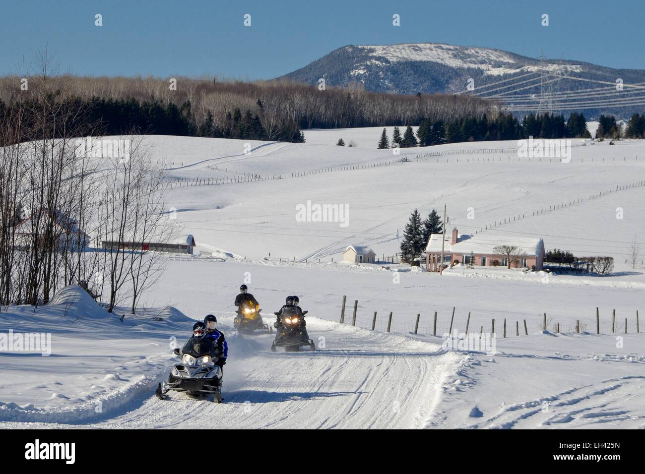 Canada, Quebec province, region of Charlevoix, Baie Saint Paul, column of snowmobiles in single file on a track marked out with a house and a background mountain Stock Photo