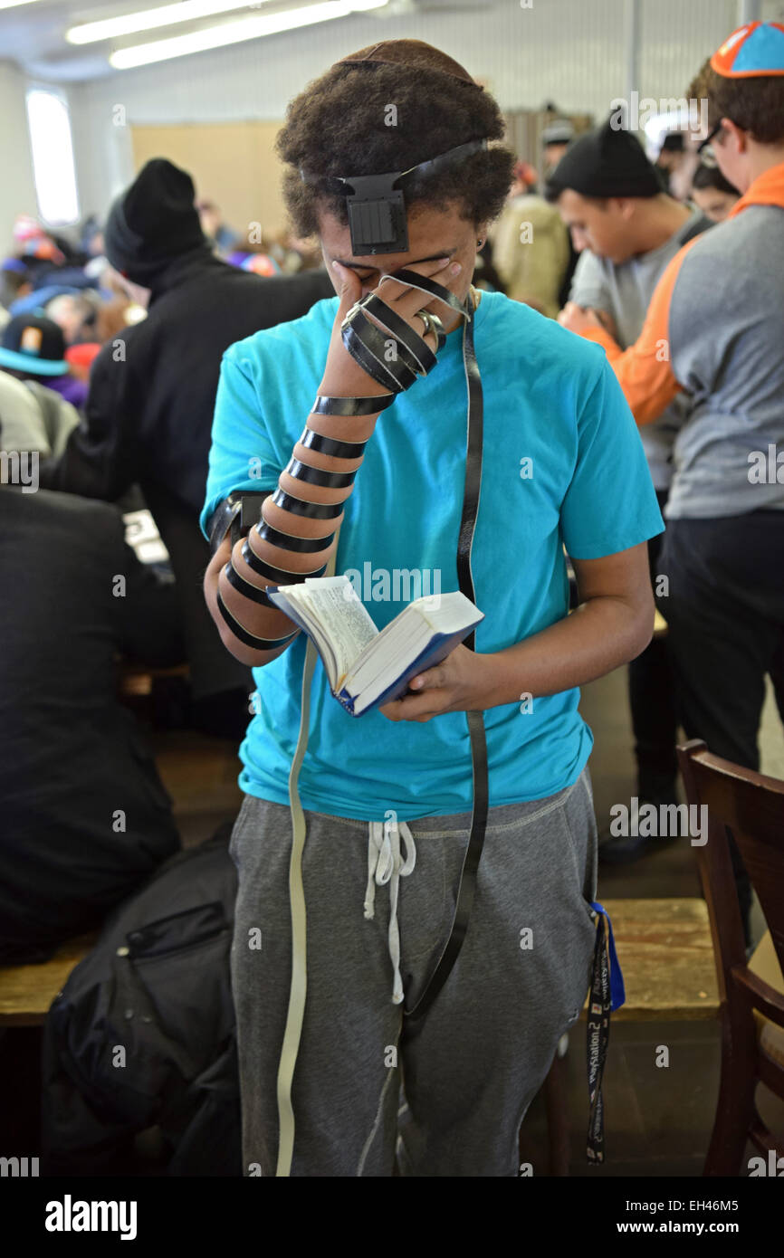 A Jewish teenager praying wearing phylacteries at a Shabbaton at the Ohel in Cambria Heights, Queens, New York City. Stock Photo