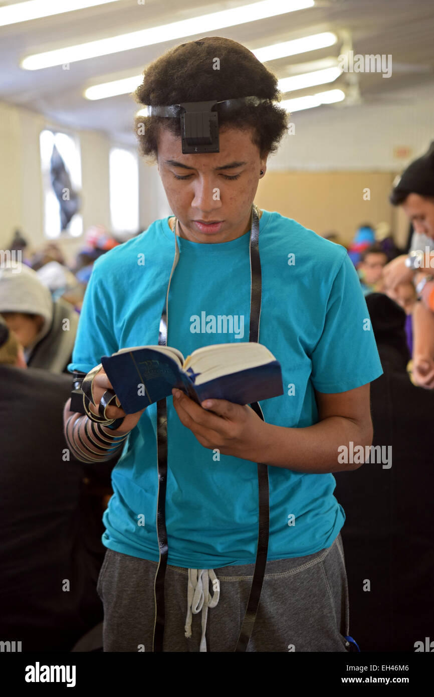 A Jewish teenager praying wearing phylacteries at a Shabbaton at the Ohel in Cambria Heights, Queens, New York City. Stock Photo