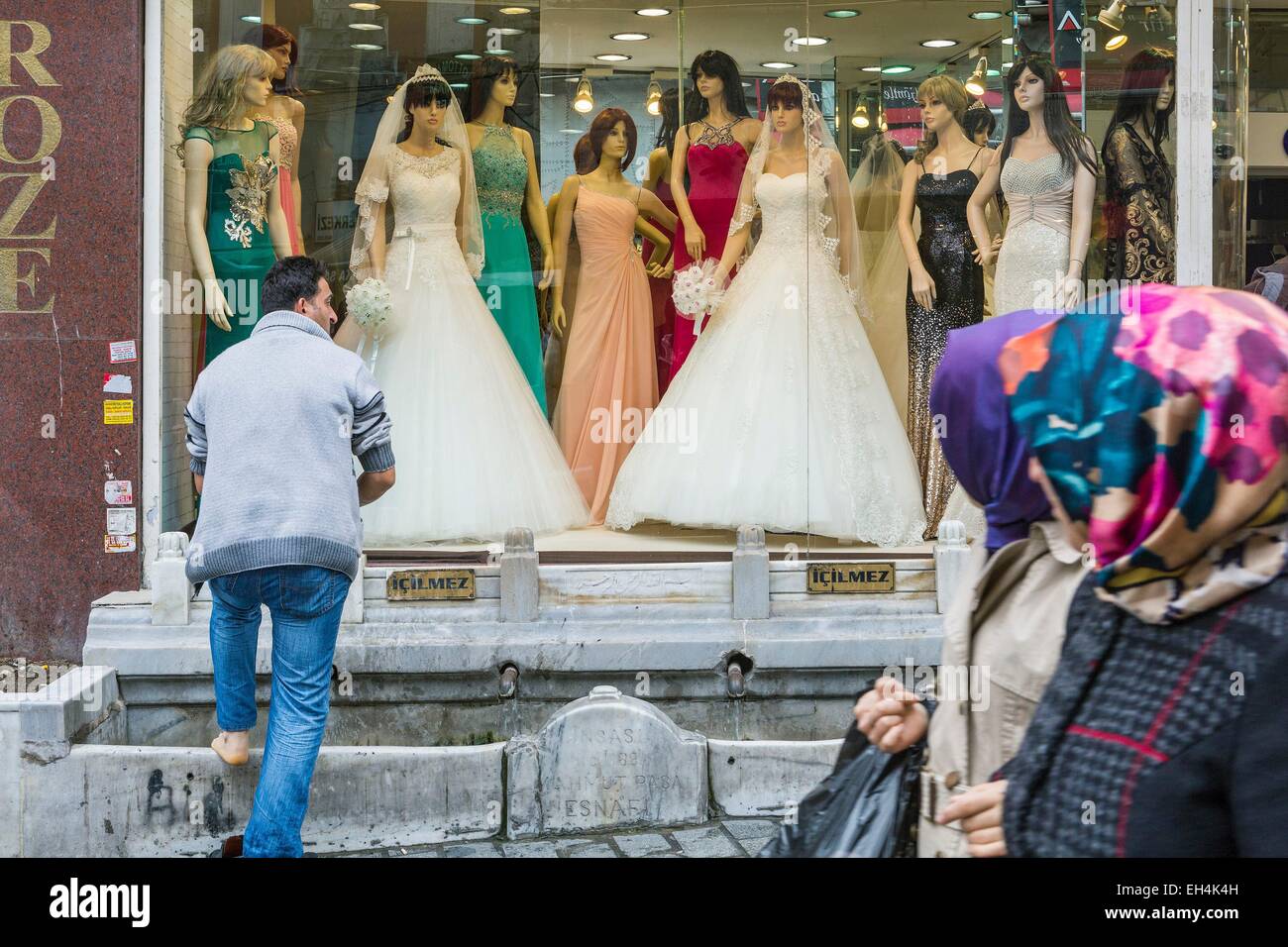 Turkey, Istanbul, Mercan, Turkish man washing his feet in a fountain in front of the window of a wedding dress store Stock Photo