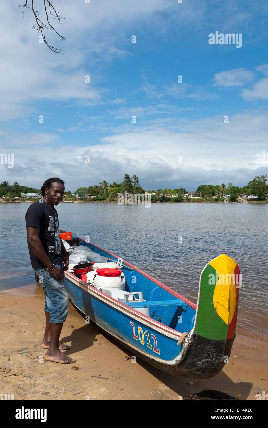 Republic of Suriname, Lawa River becoming downstream the Maroni River, pirogue in charge and stranded on the shore side Suriname, portrait of a boatman (Seke), in the background the village of Grand-Santi Stock Photo