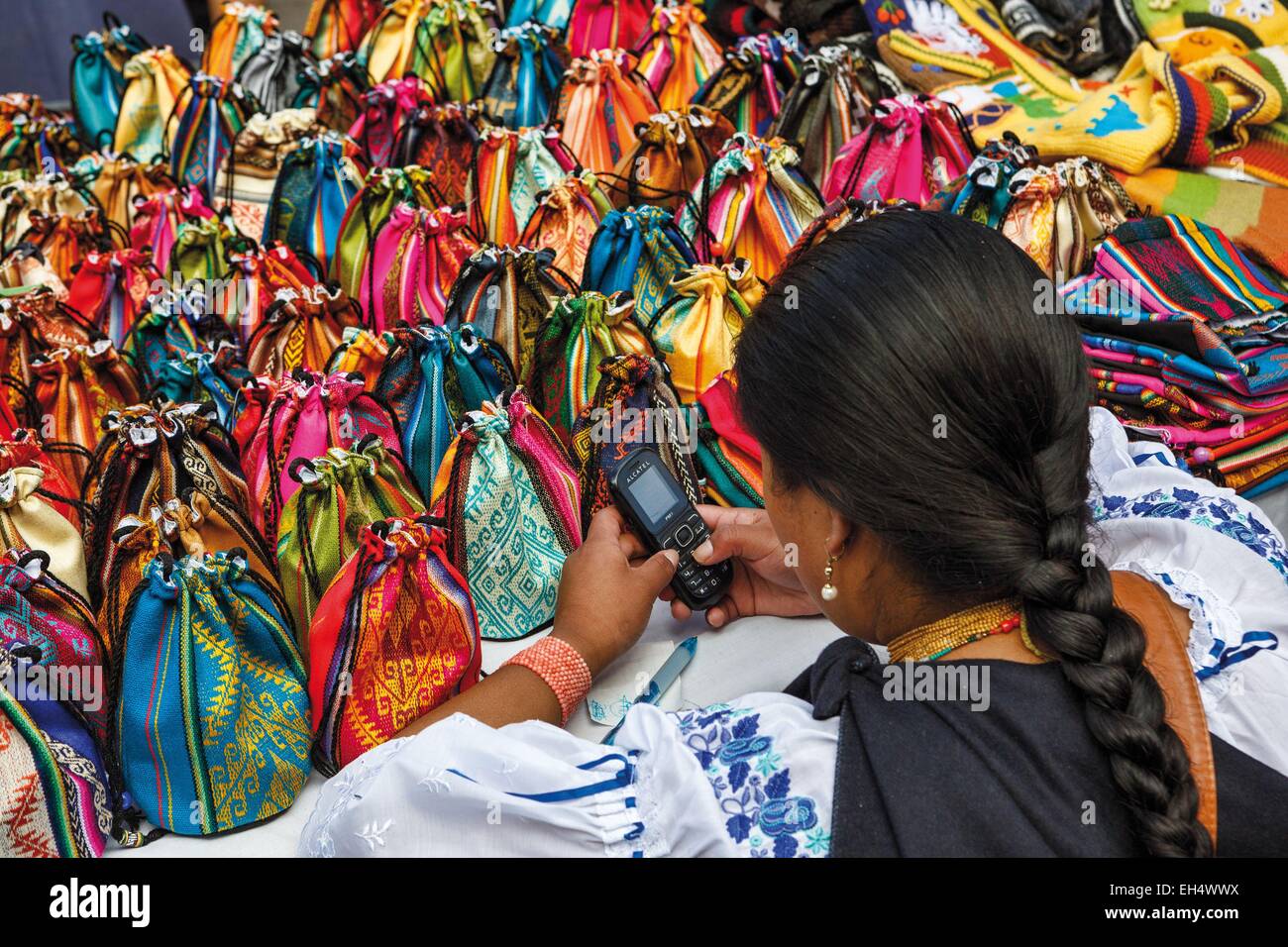 Ecuador, Imbabura, Otavalo, young saleswoman typical handicraft bags, dressed in a traditional way, using a mobile phone Stock Photo