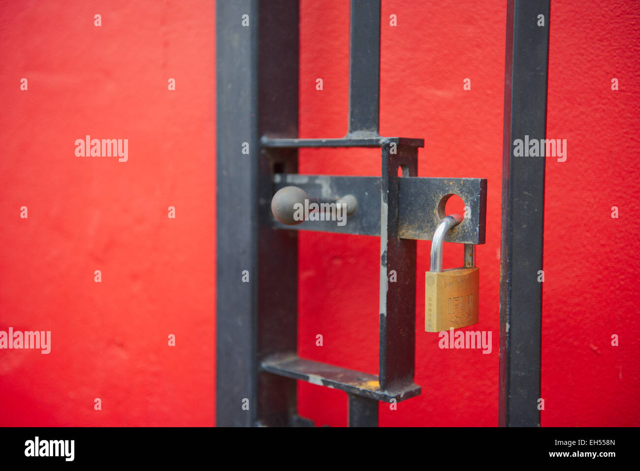 Padlock locked on open bolt in metal gate in front of red wall Stock Photo