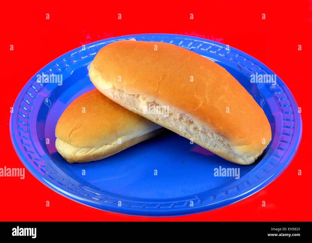 Hot dog bun on a blue plate on a red background. Stock Photo