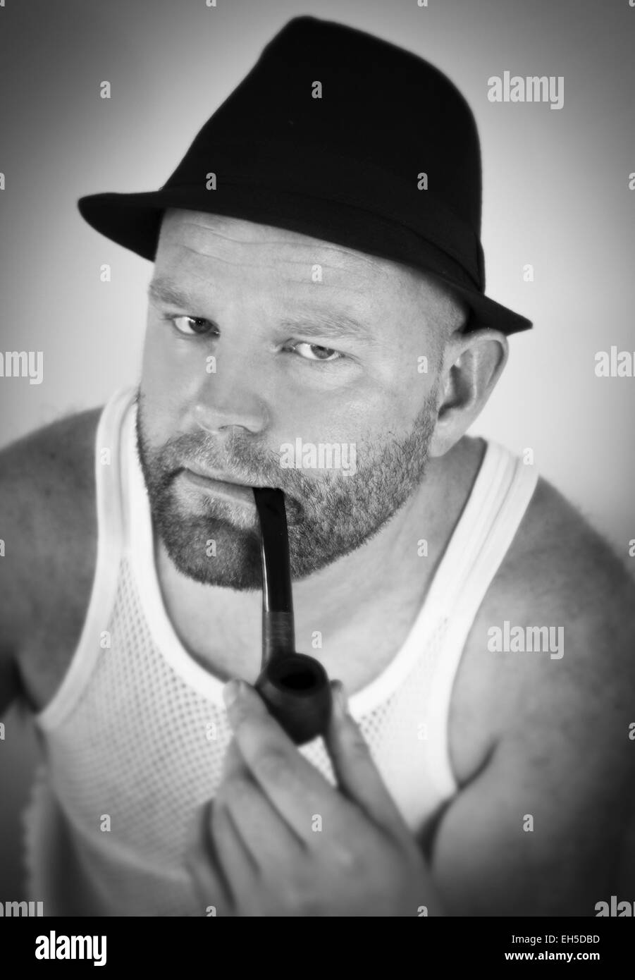 Man smoking tobacco pipe, with hat and singlet. Stock Photo