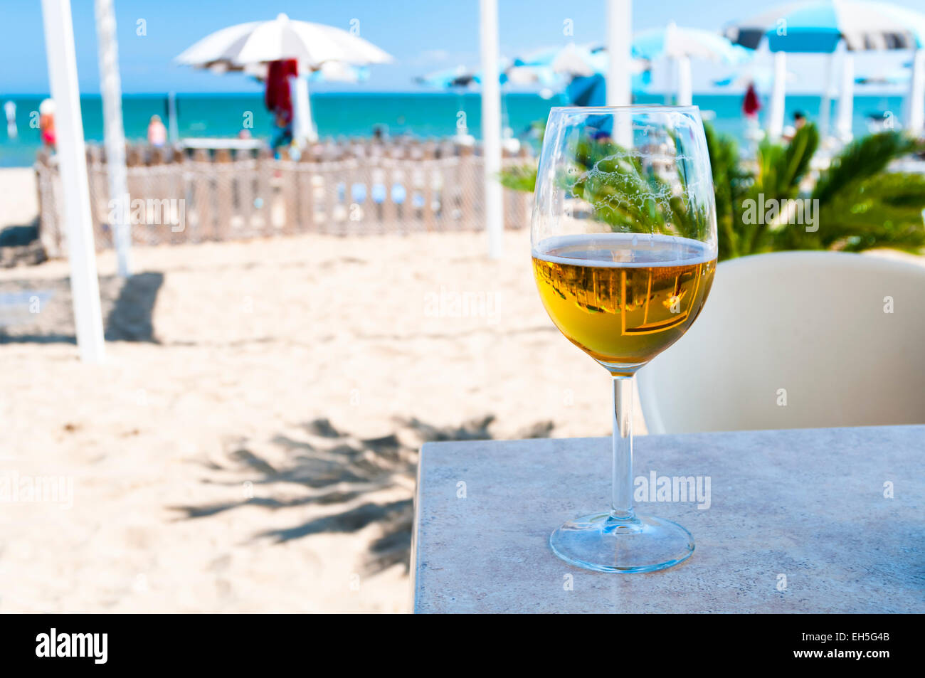 Half empty glass of beer in shadow on sandy beach Stock Photo