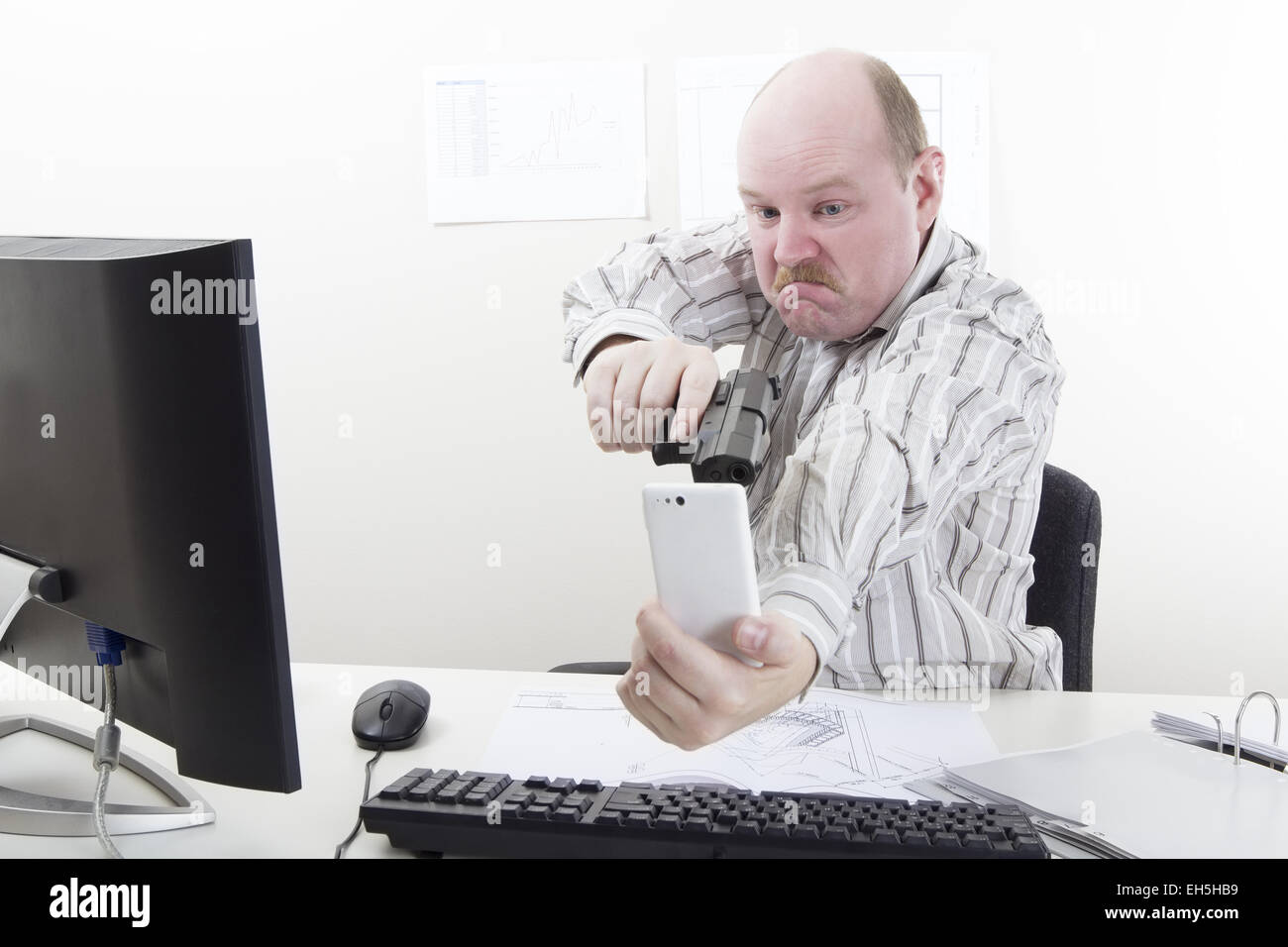 Man points a gun at his mobile / cell phone in his office. Stock Photo