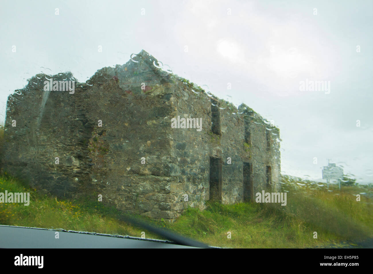 View through rainy window of car (with the window wipers in motion) of an old dilapidated stone cottage in Ireland Stock Photo