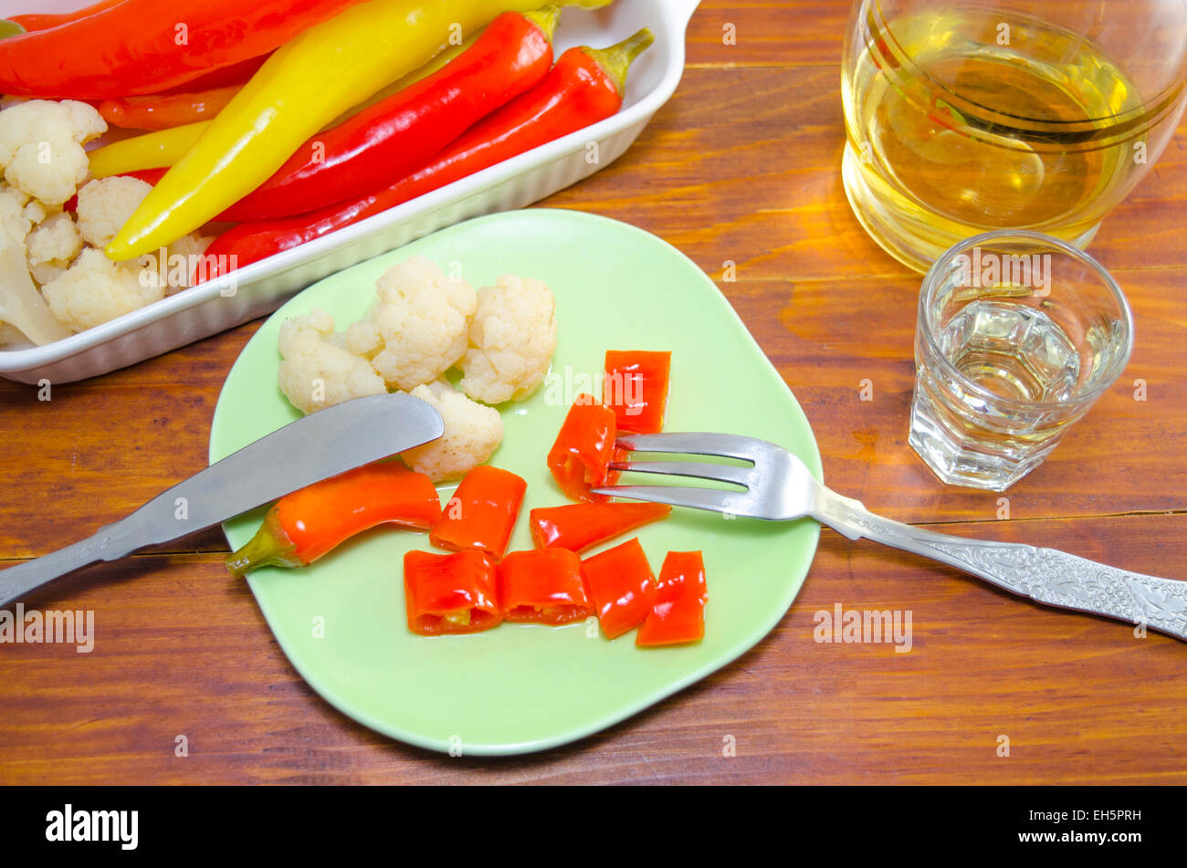 Pickled peppers, cauliflower and olives on a plate with a knife and a fork and a shot of brandy Stock Photo