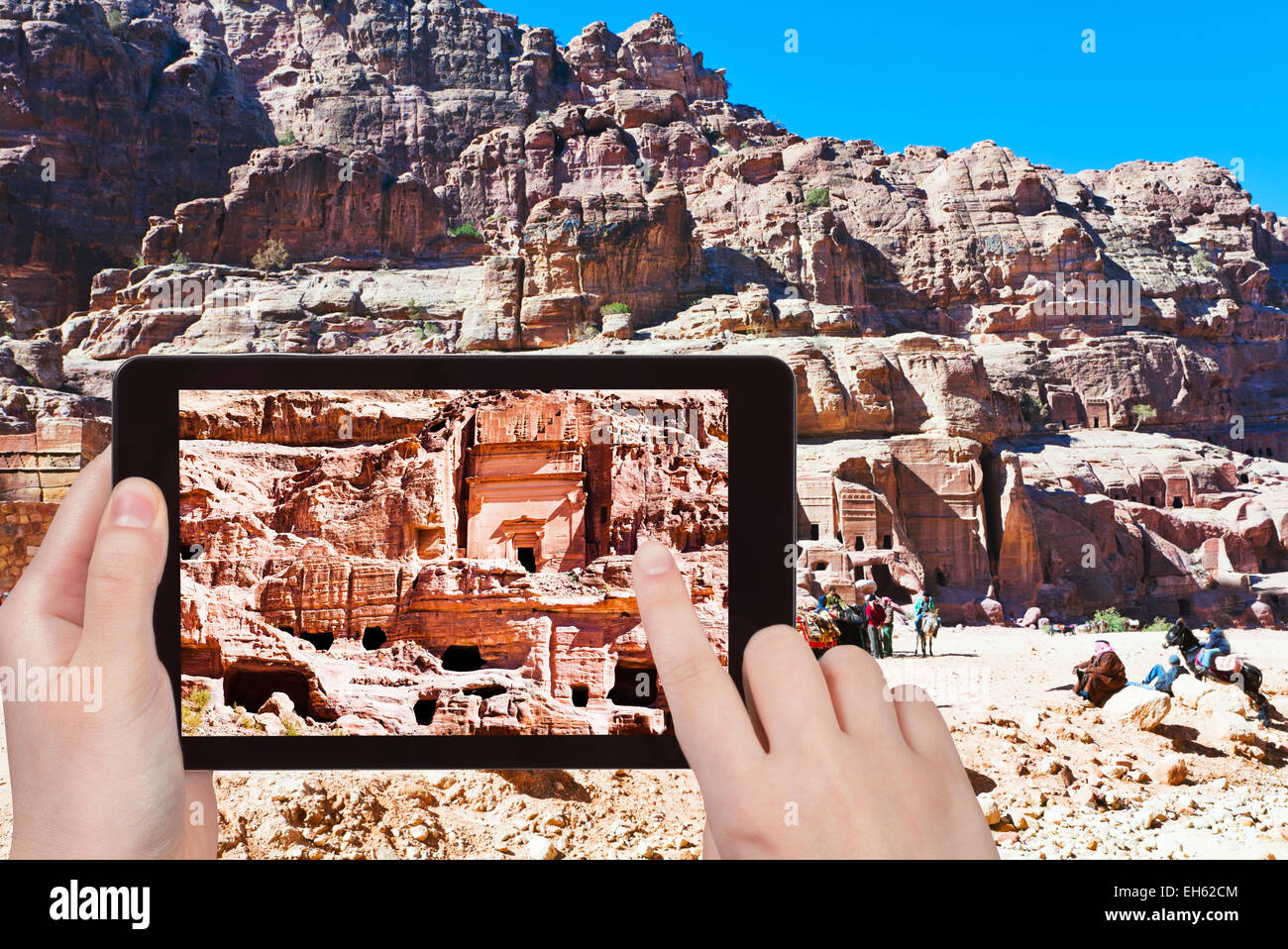 travel concept - tourist taking photo of tombs and houses in stone city Petra, Jordan on mobile gadget Stock Photo