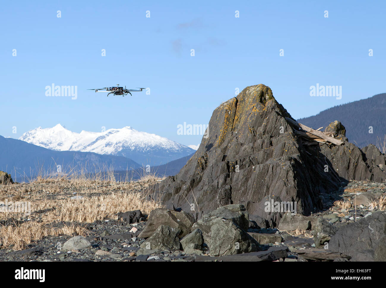 Quadcopter drone flying over rocks on a Southeast Alaskan beach on a sunny day. Stock Photo