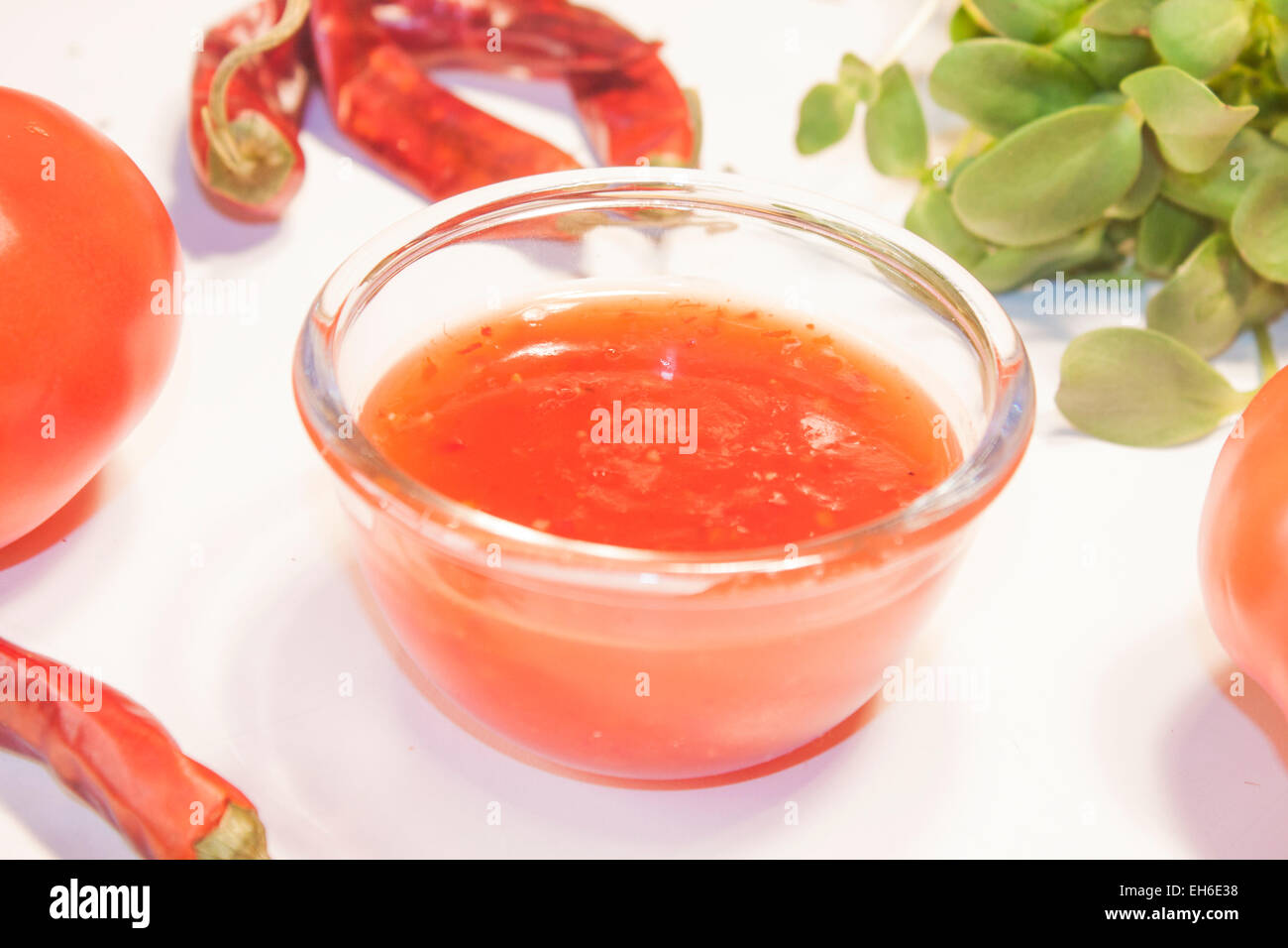 A glass full of thai sweet chili sauce, between chilis and tomatoes Stock Photo