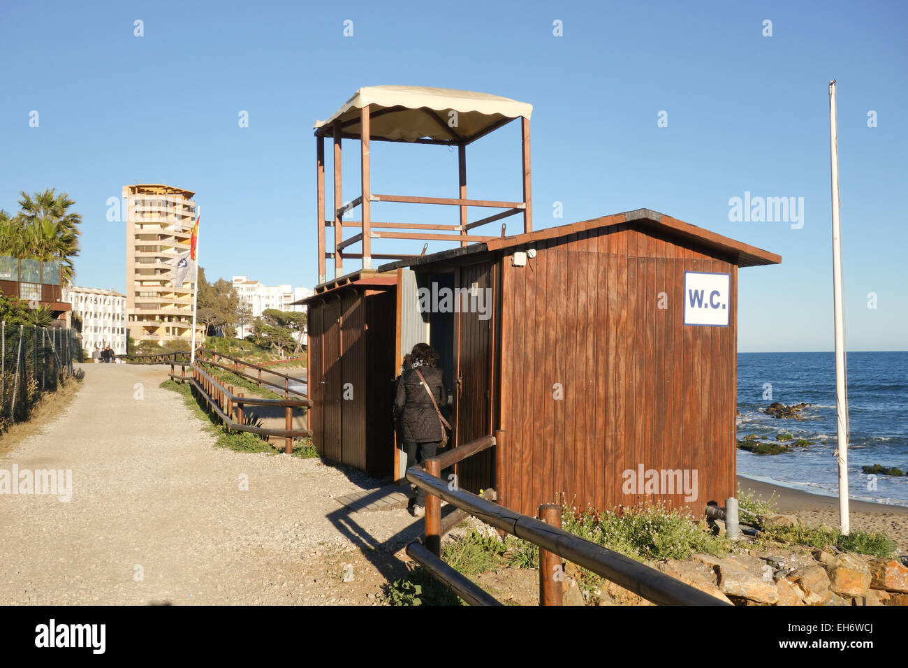 Woman entering Public toilet, WC, on beach at wooden boardwalk, seafront promenade, Costa del Sol, Andalusia, Spain. Stock Photo