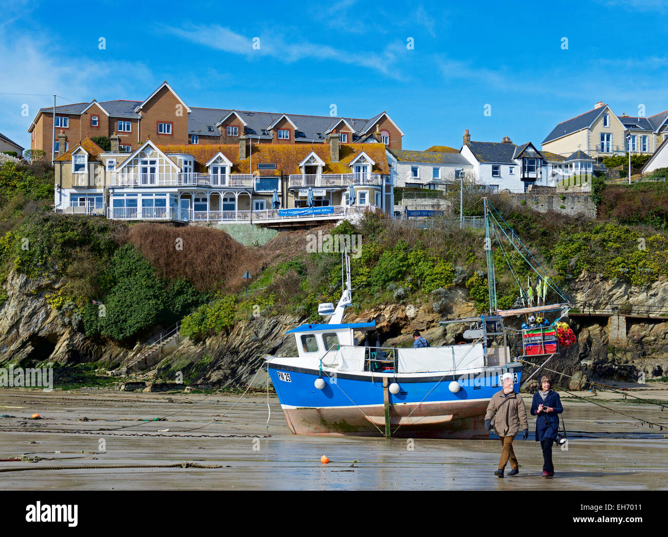 Couple walking past fishing boat on beach in harbour, Newquay, Cornwall, England UK Stock Photo