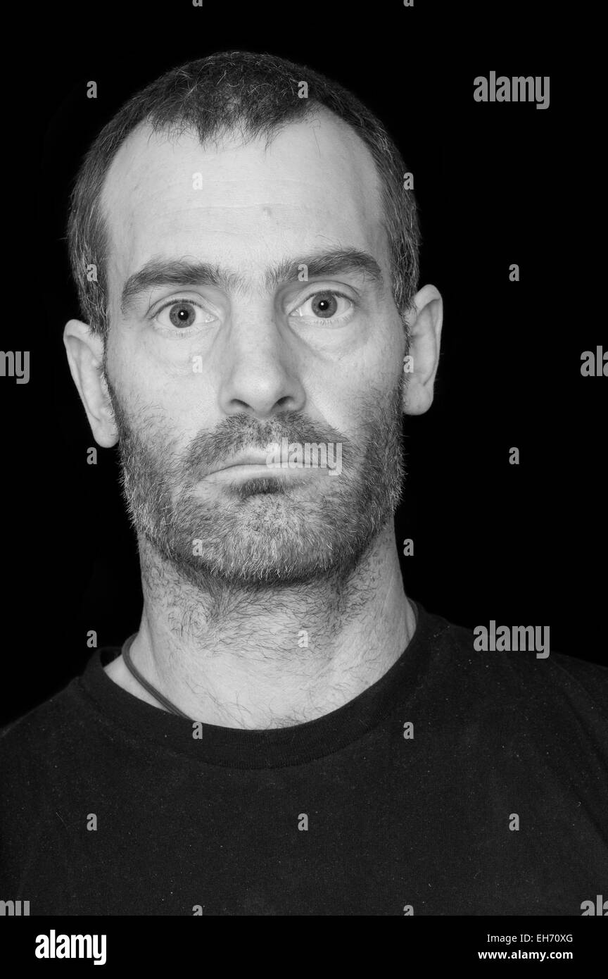 black and white portrait of a rugged grizzled middle aged man with black t-shirt on black background Stock Photo