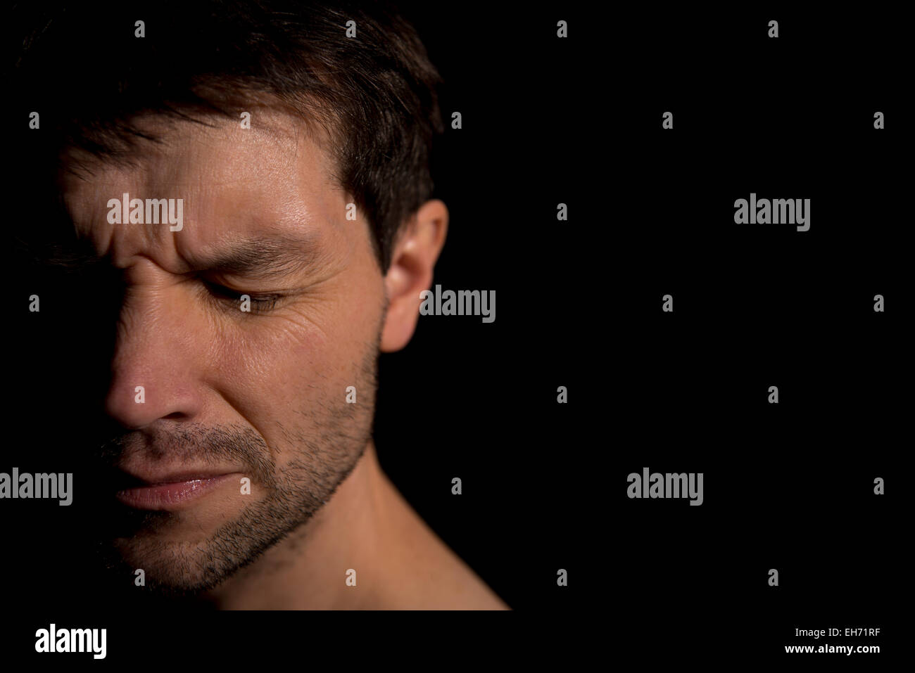 Close up portrait of an unshaven man, with his eyes closed tight and suffering with emotional pain. Stock Photo