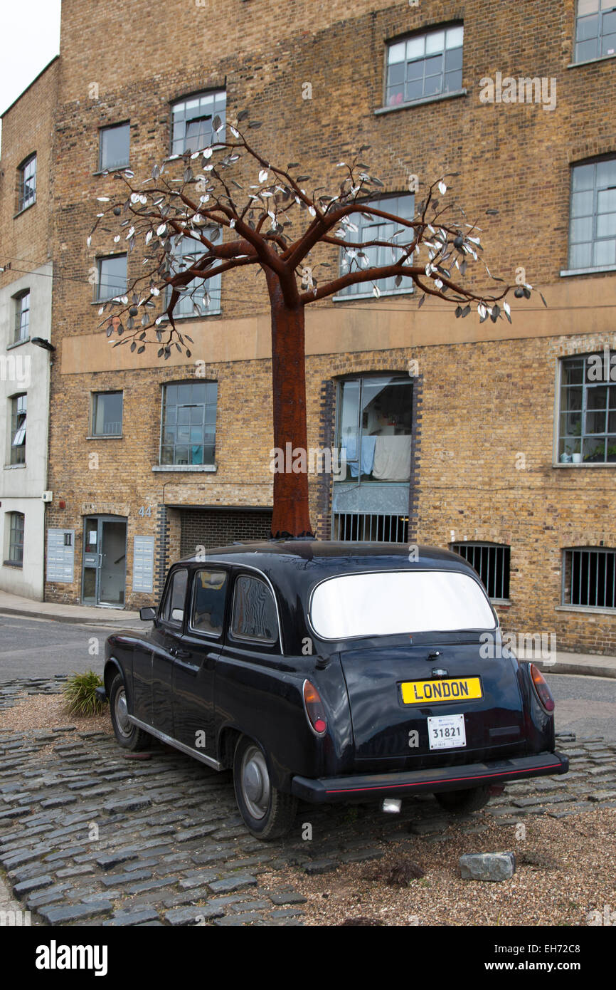 A sculpture of a taxi with a metal tree growing through it by Andrew Baldwin on a roundabout, Orchard Place, London, UK. Stock Photo
