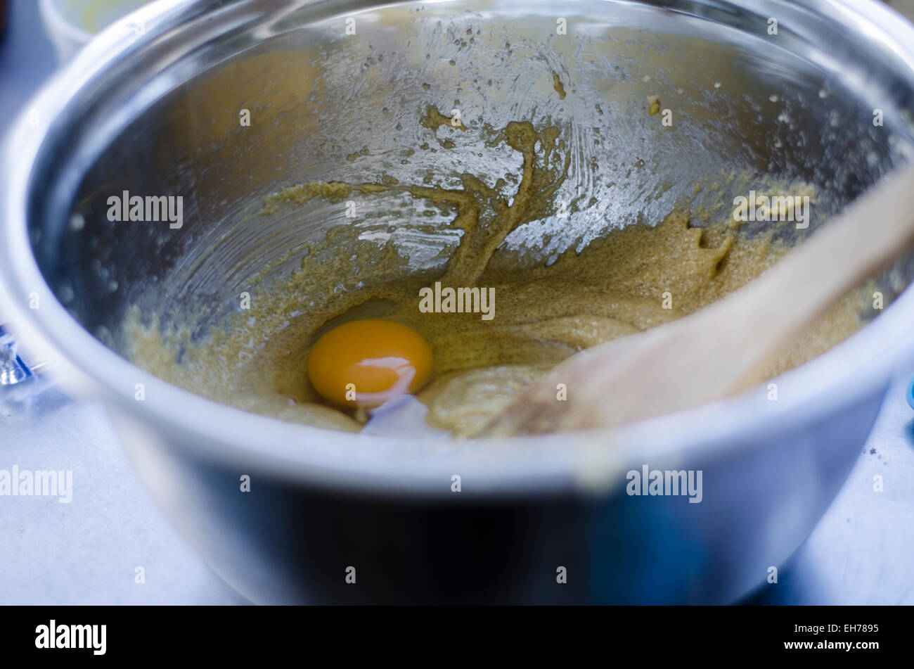 Adding an egg to the cake mix with a wooden spoon going to mix it up. egg is in focus. Stock Photo
