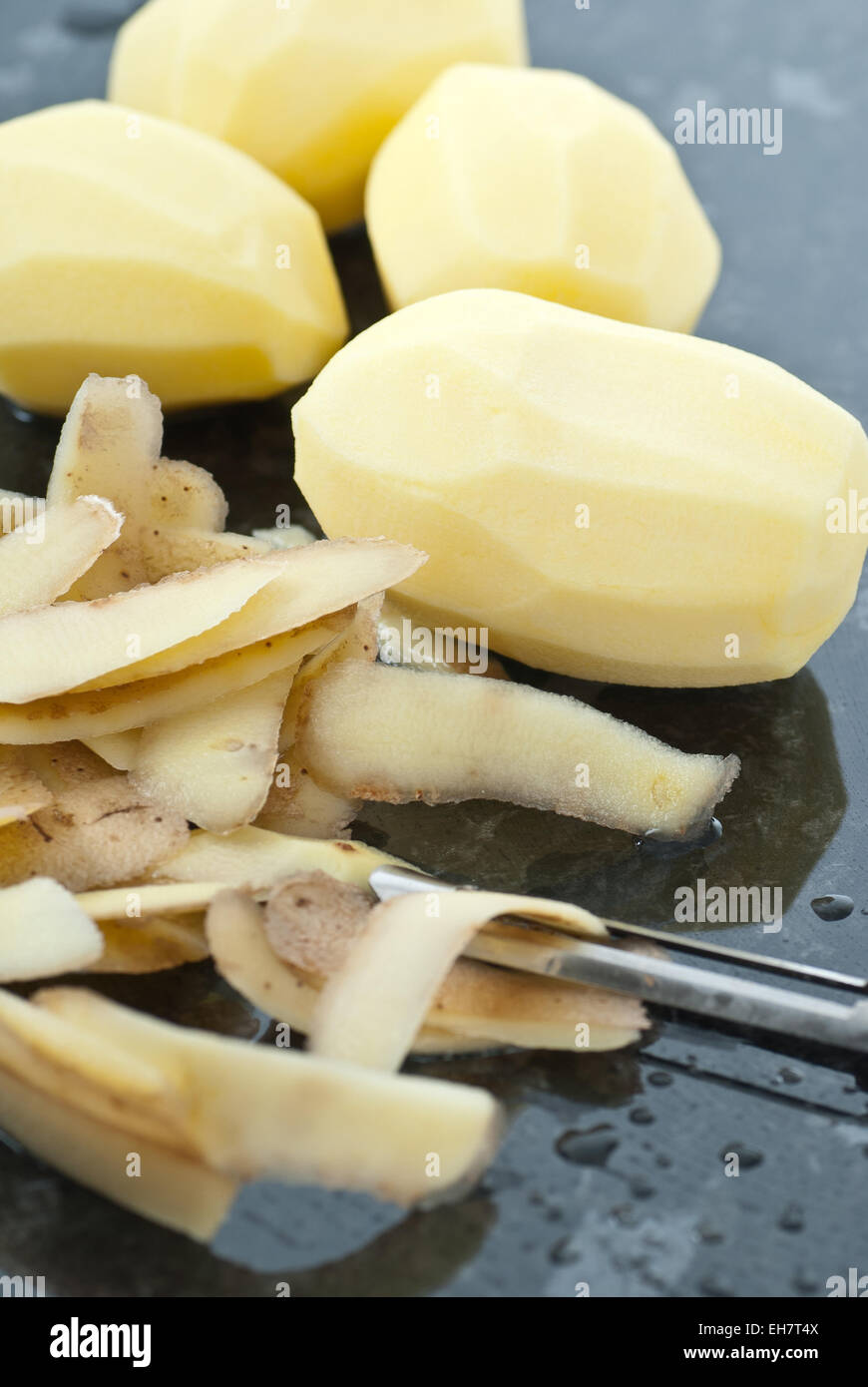 Raw peeled potatoes with peeler. Stock Photo