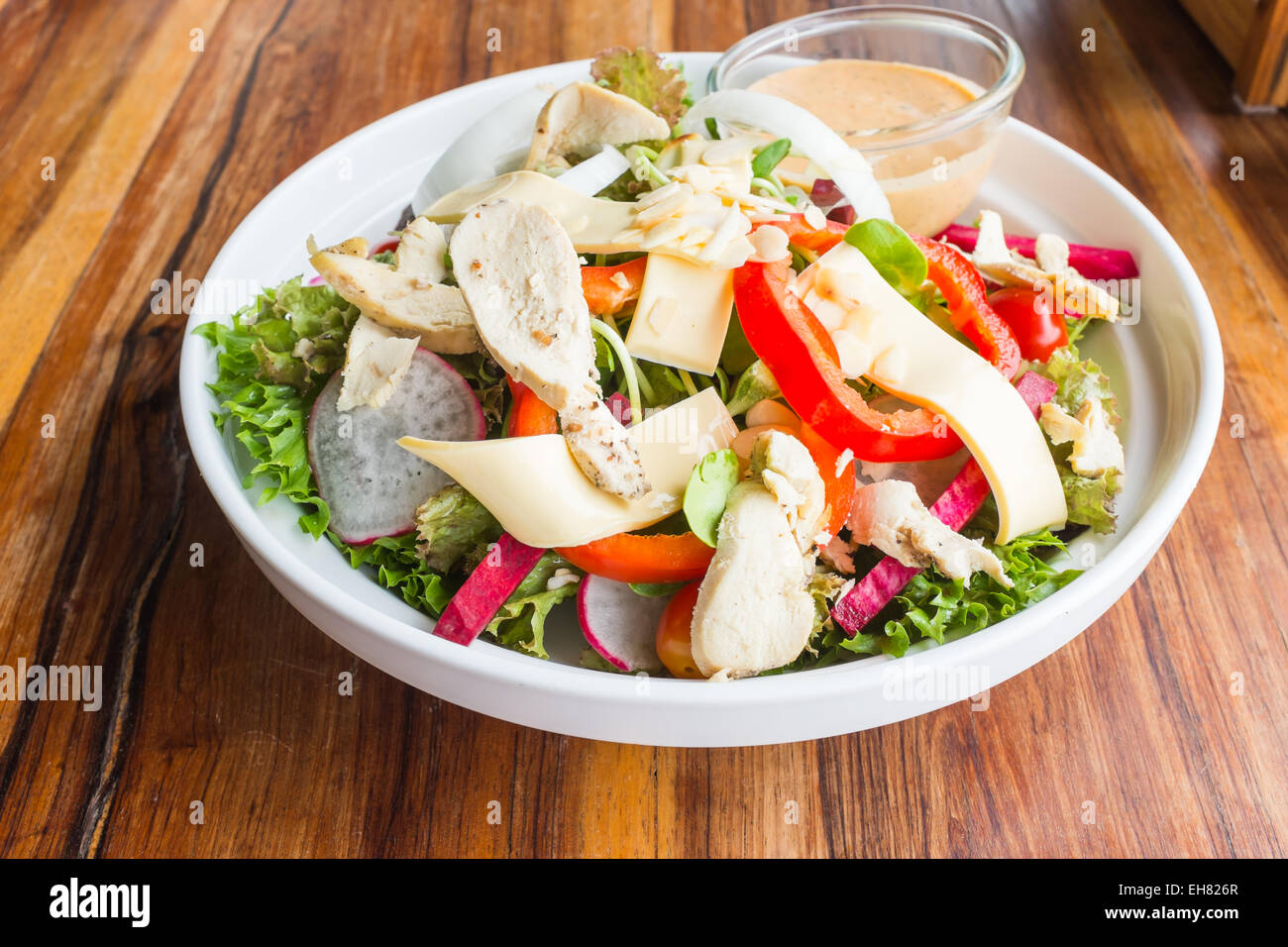 chicken cheese and vegetables salad with caesar dressing souce in white dish on wood table in restaurant Stock Photo