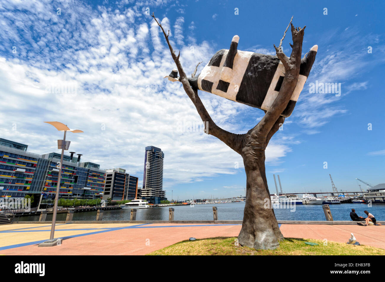 Surreal sculpture of a dead cow stuck up a tree - public art in Melbourne Docklands, Australia, an urban regeneration area. Stock Photo