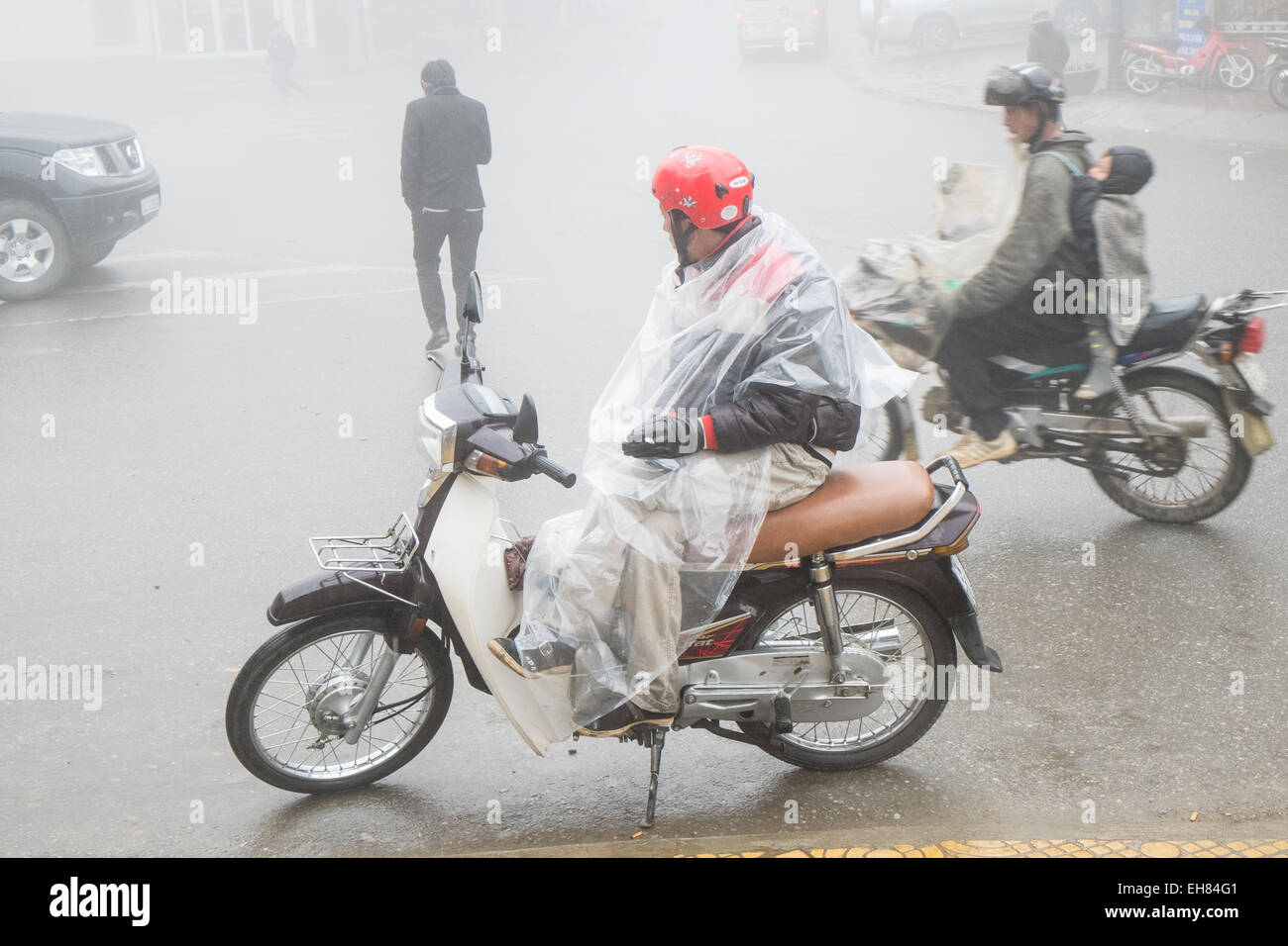 Scooter taxi rider smokes while he waits for a fare on a wet and foggy day in hill tribe town of Sa Pa,Sapa,Vietnam, Stock Photo